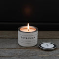 Mini Petaluma berry candle by backhouse burning against a dark background, with a visible flame and warm glow.