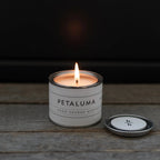 Mini Petaluma berry candle by backhouse burning against a dark background, with a visible flame and warm glow.
