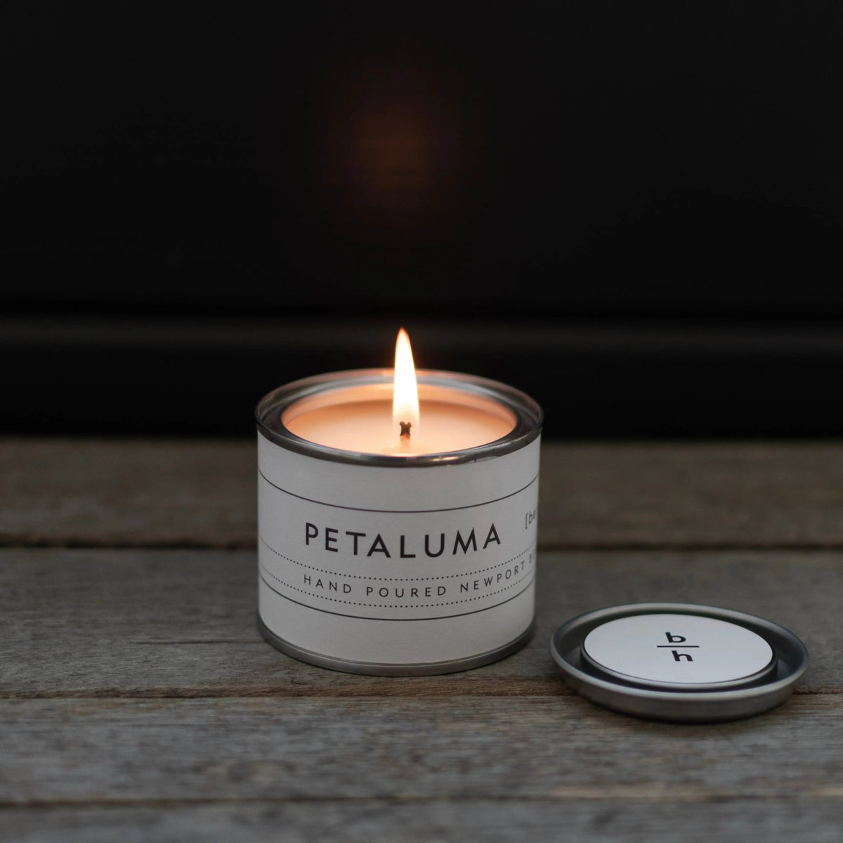 Mini Petaluma berry candle by backhouse burning against a dark background, with a visible flame and warm glow.