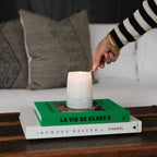 A white LIDO scented candle being lit with a match, sitting atop stacked fashion books including La Vie de Clare V. and Jacques Helleu & Chanel on a vintage trunk Newport Beach