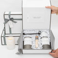 A backhouse hand poured Newport Beach candle gift set featuring Mr Douglas pine and Apolena sea salt scented candles with matches in an elegant white gift box with black and white striped ribbon, alongside a lit Grove candle.