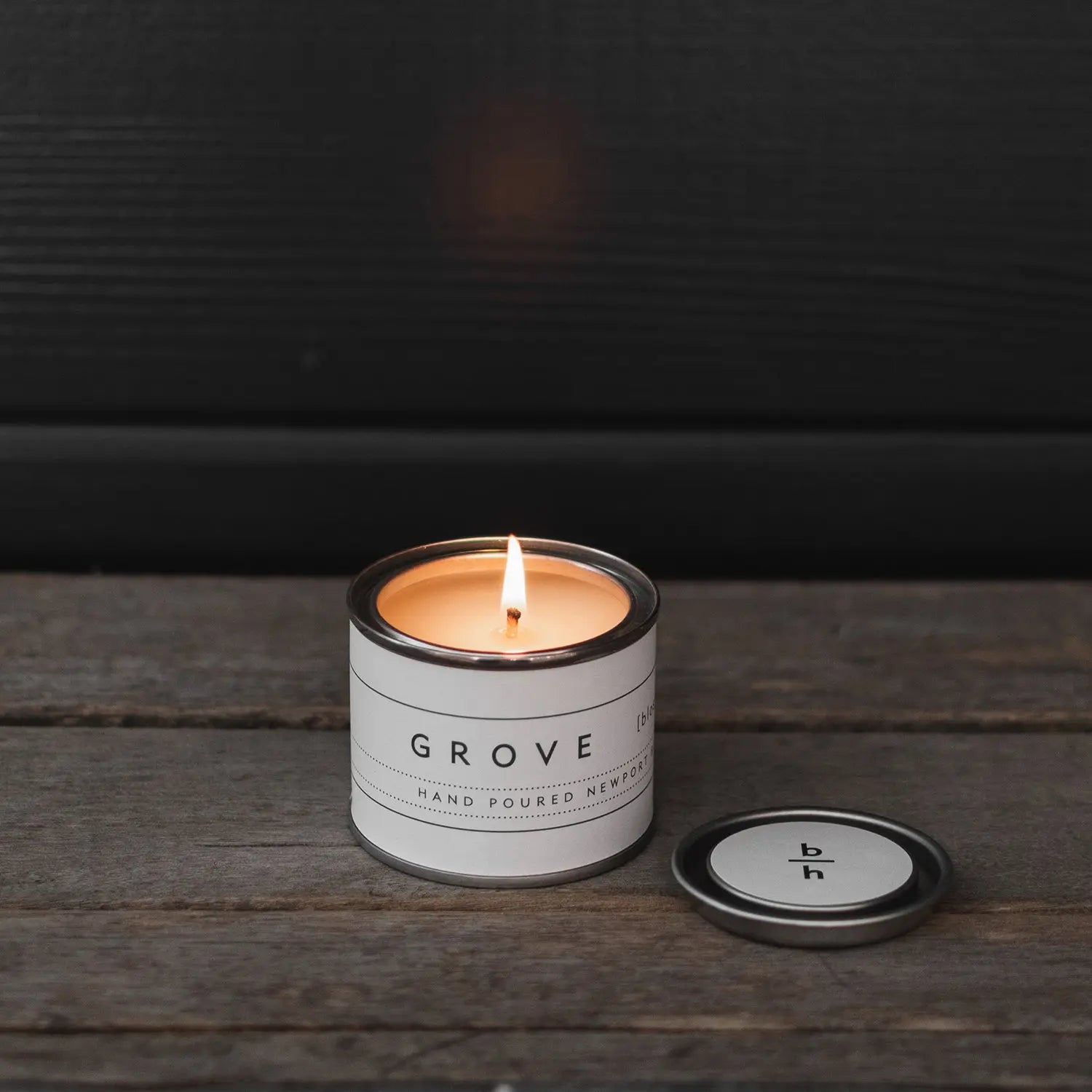 Mini Grove orange blossom candle by backhouse burning against a dark background in its classic glass vessel.