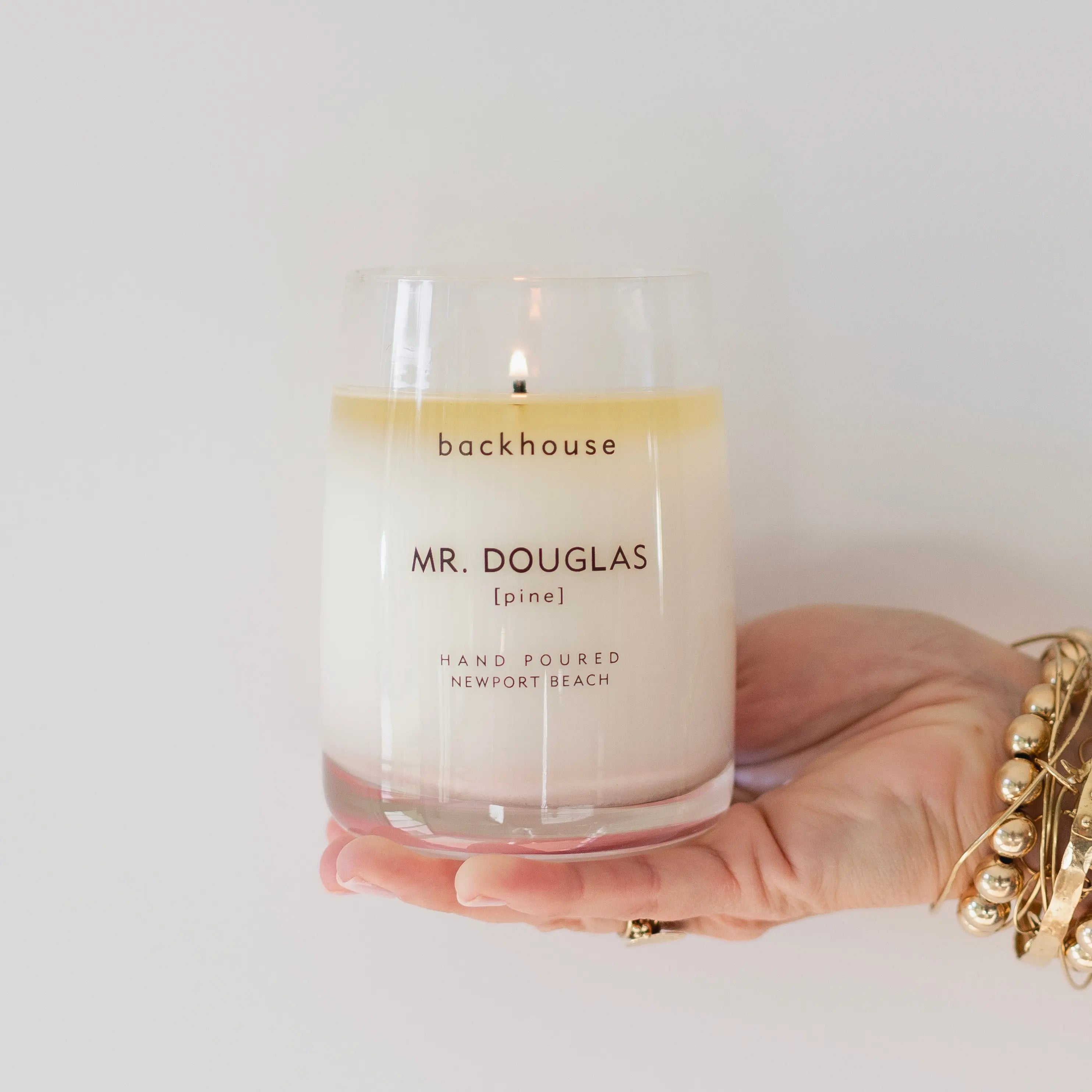 Mr. Douglas pine candle by backhouse lit and held in hand against a white background, shown in its classic glass vessel.