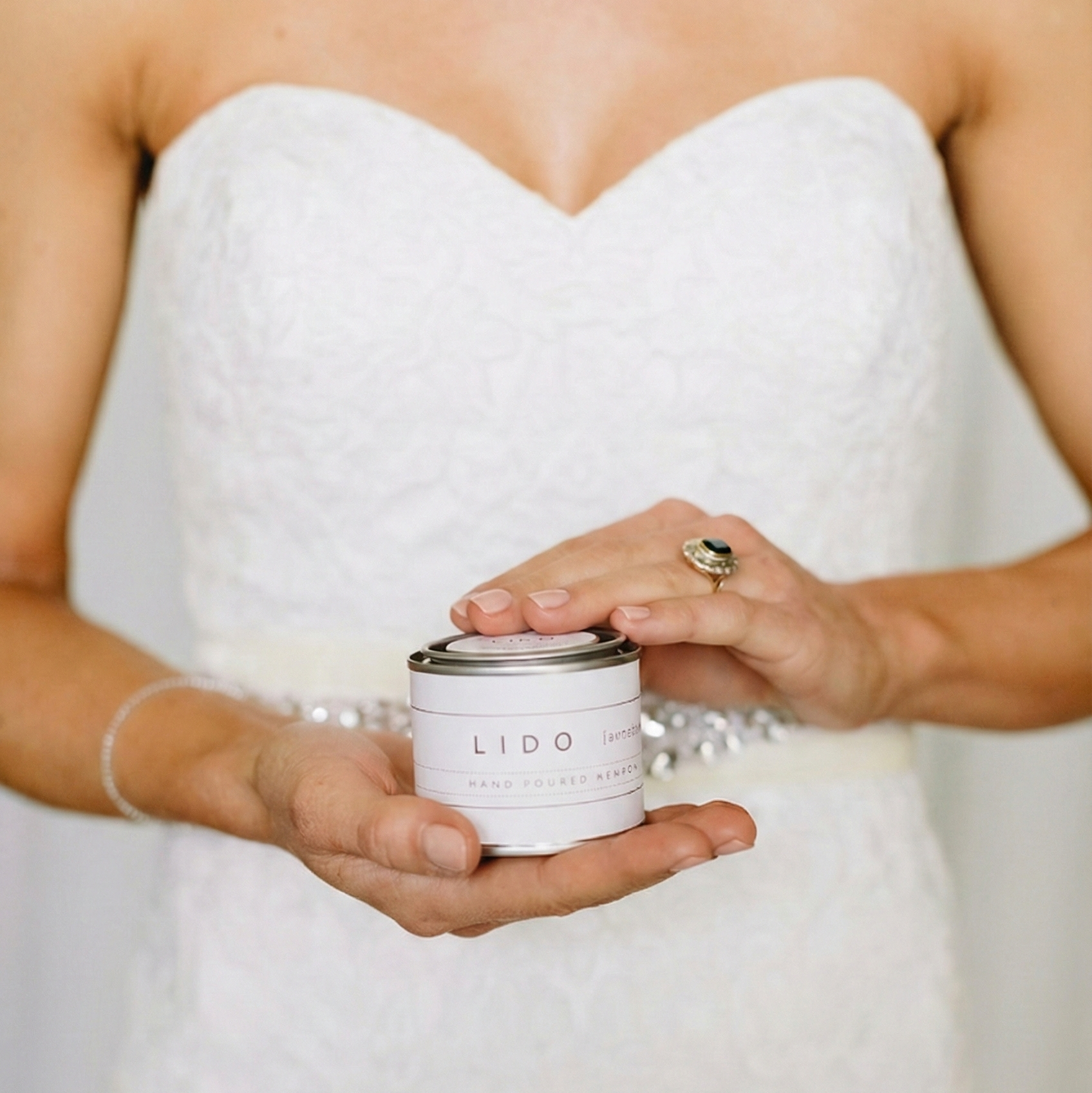 Bride in a white lace dress holding a Lido Newport custom hand-poured mini candle wedding favor.