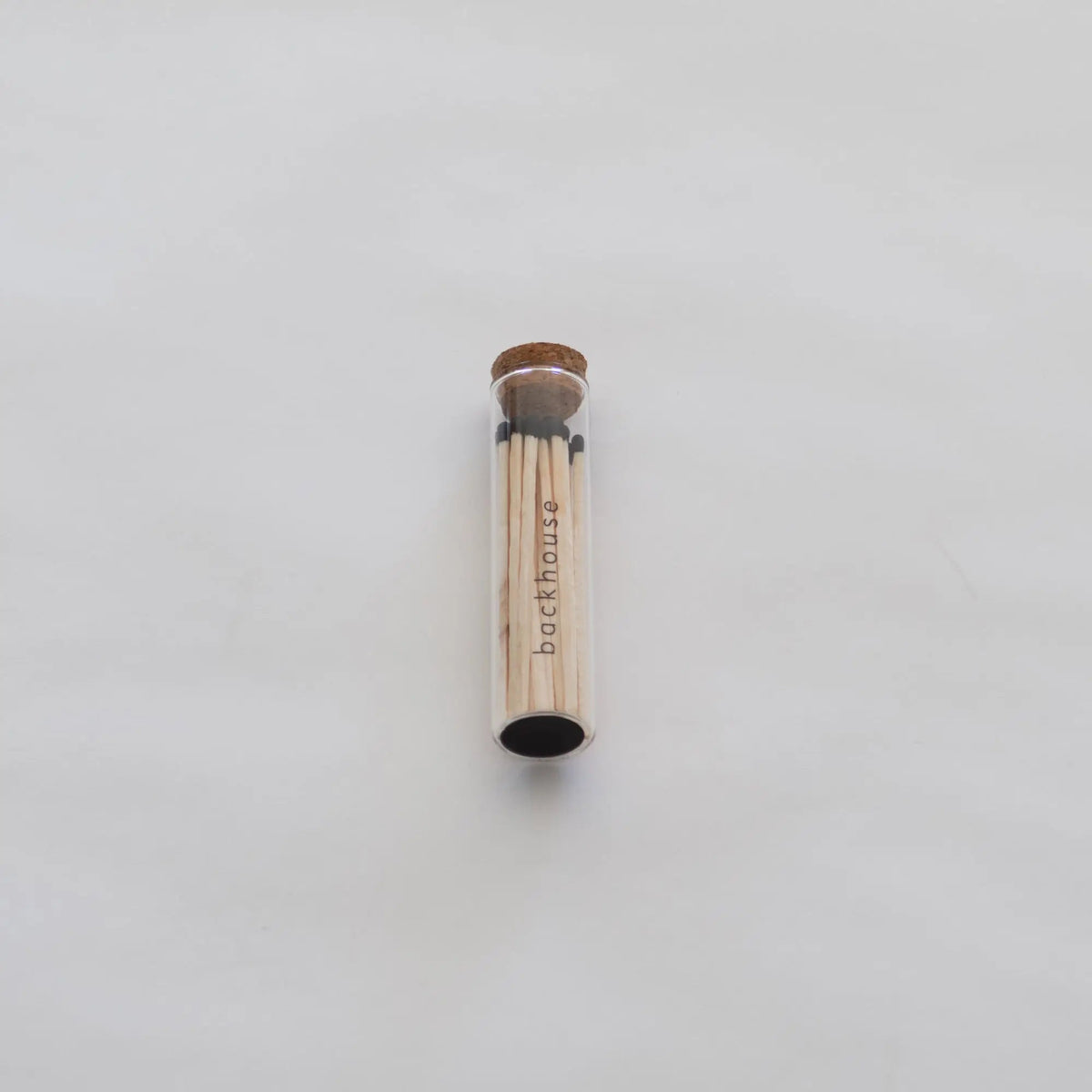 Glass tube of matches by backhouse displayed against a white background.