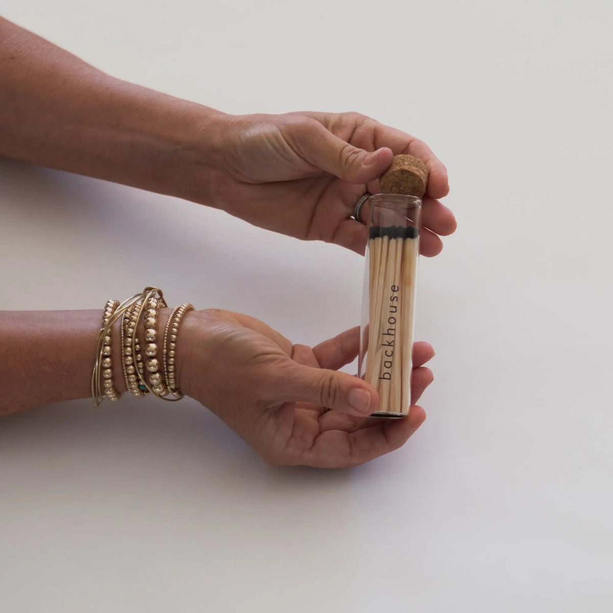 Hands holding a glass tube of matches by backhouse against a white background.