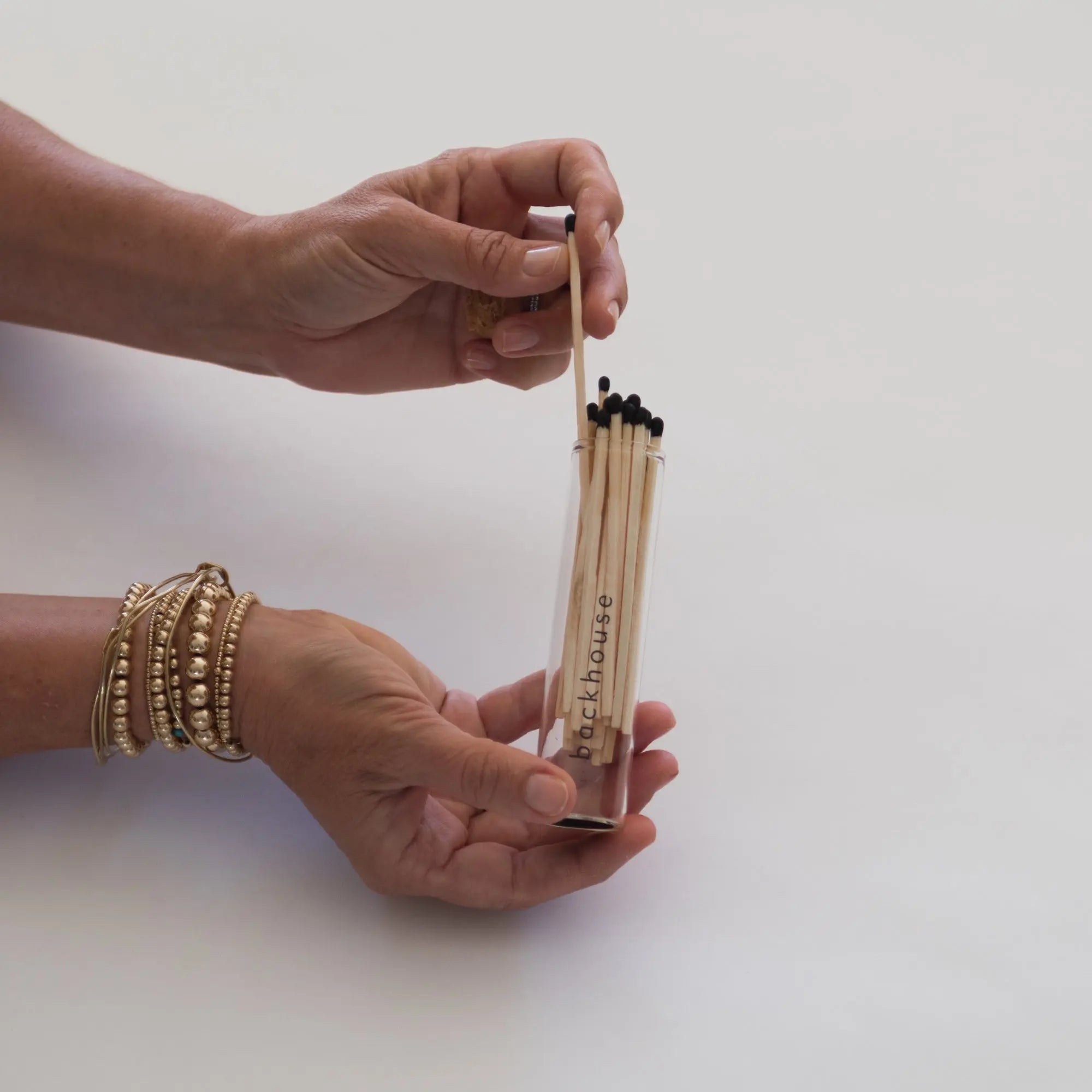 Hand removing a match from a glass tube of matches by backhouse against a white background.