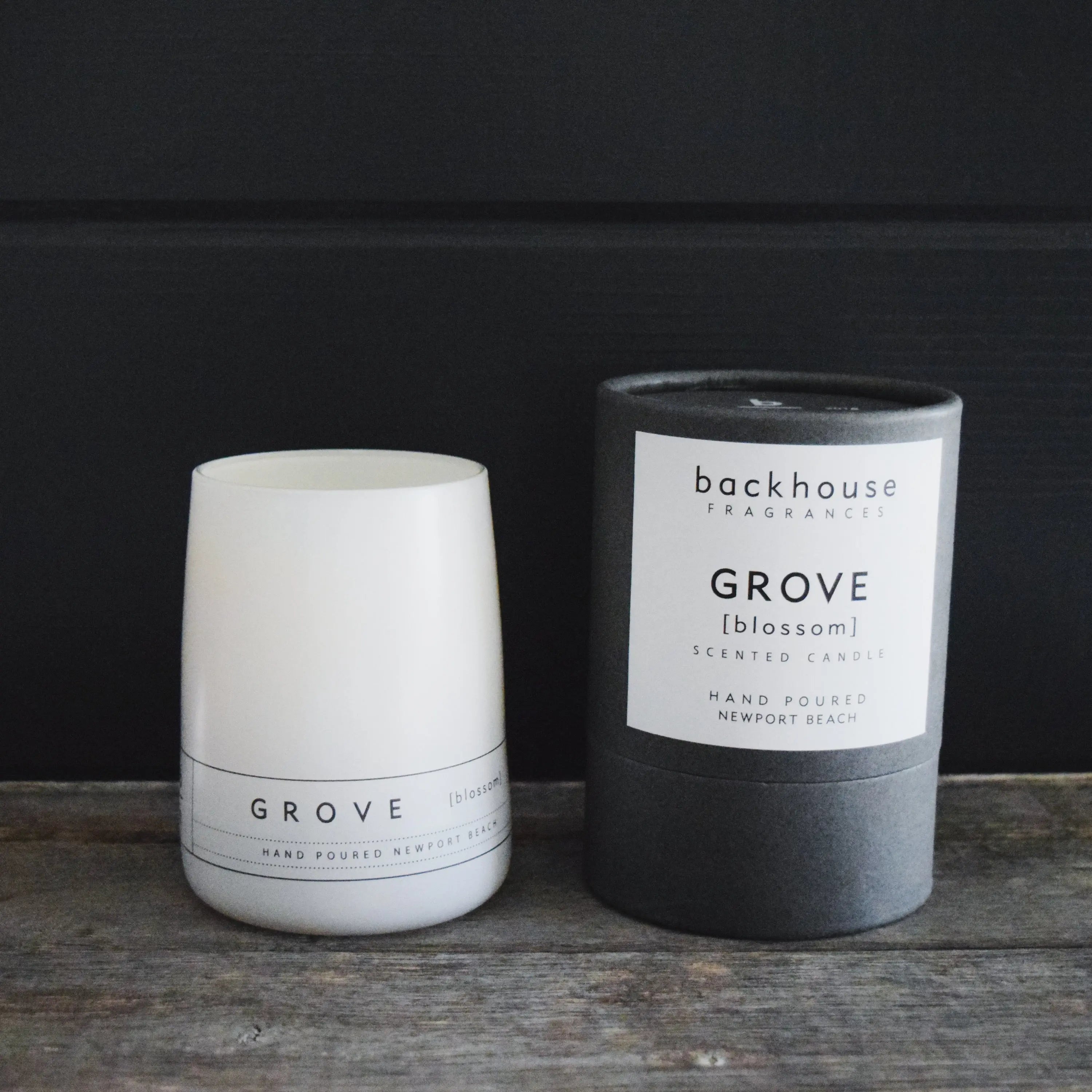Grove orange blossom candle by backhouse displayed beside its signature cylinder box against a dark background.