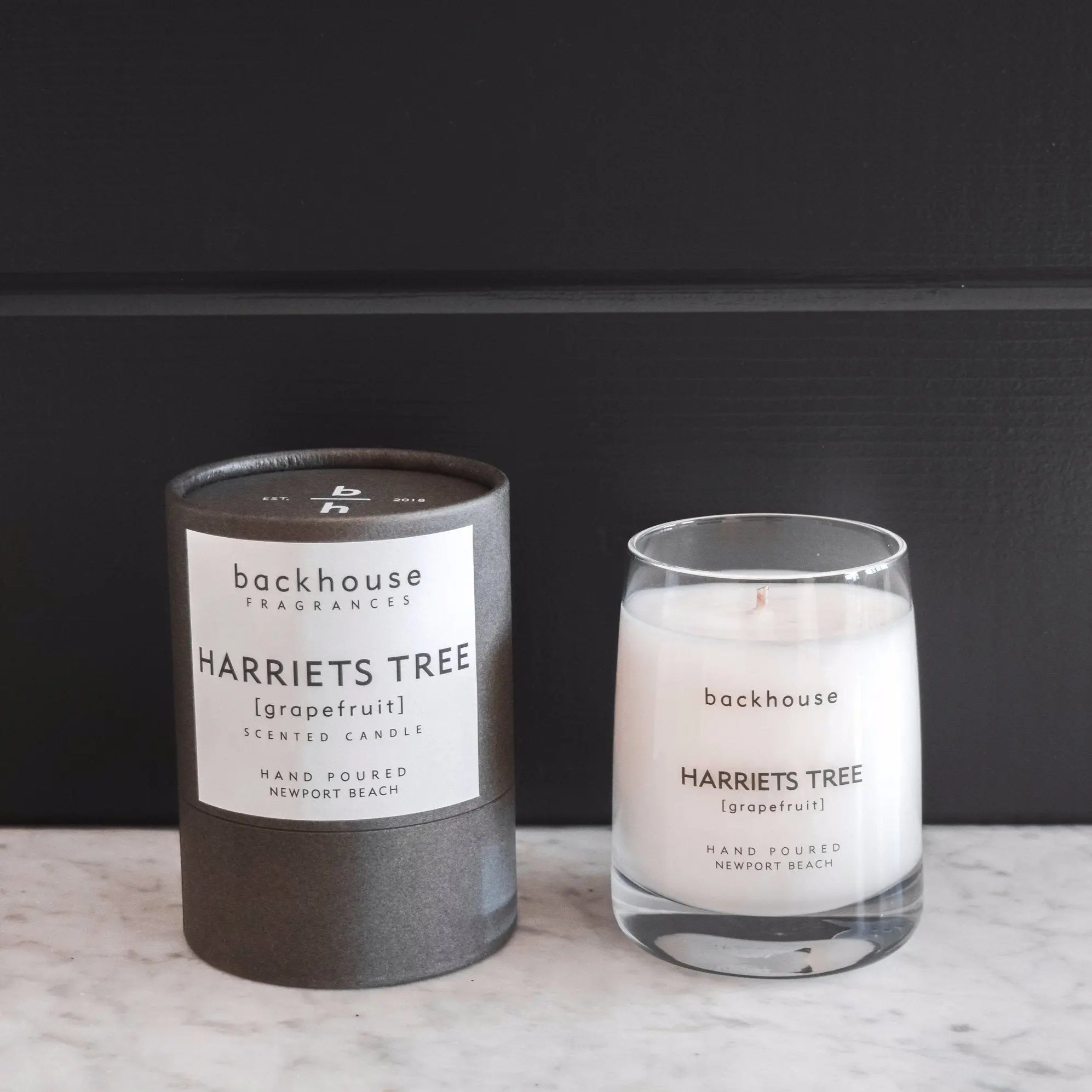 Harriets Tree grapefruit hurricane candle by backhouse displayed beside its signature cylinder box against a dark background.