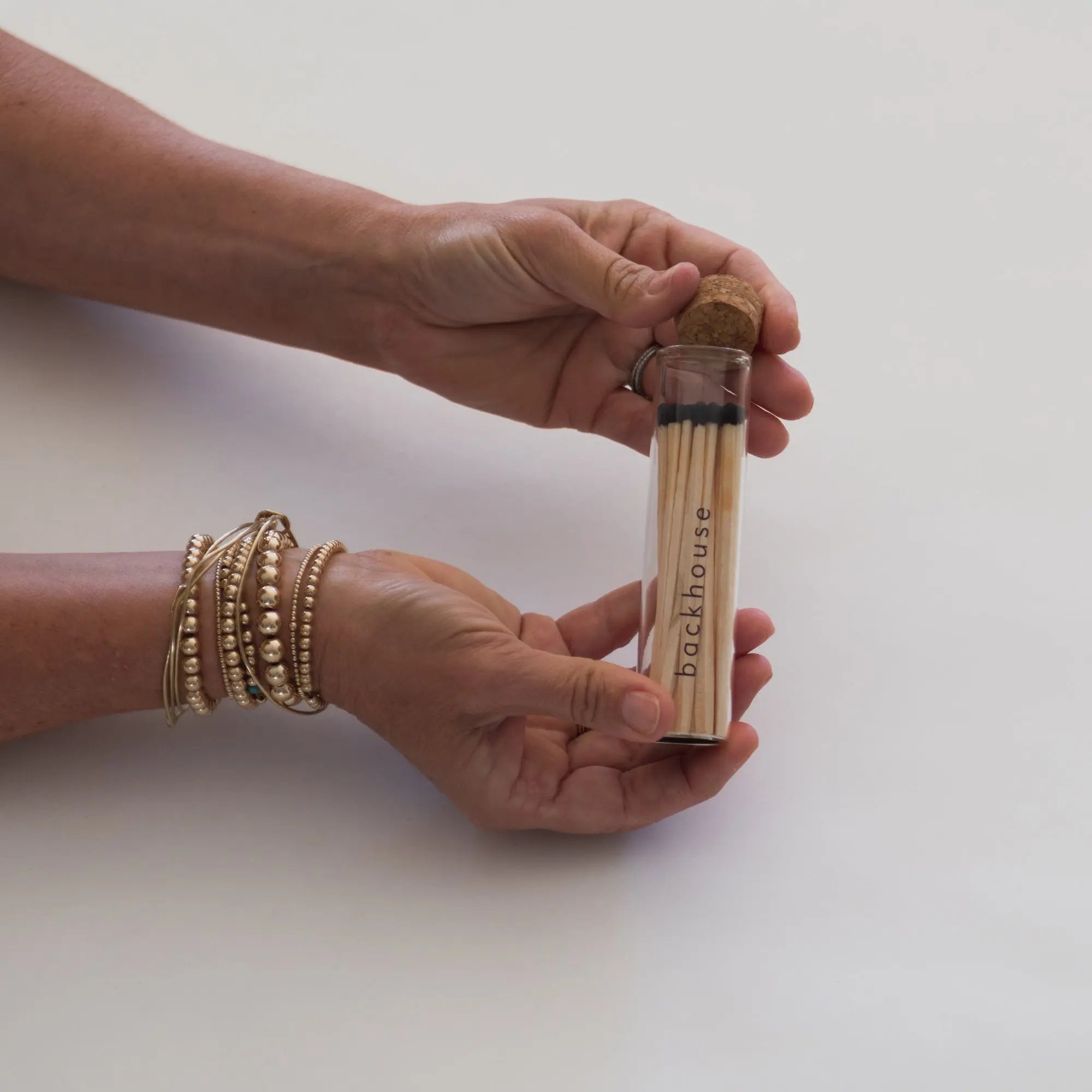 Hands holding a glass tube of matches by backhouse against a white background.