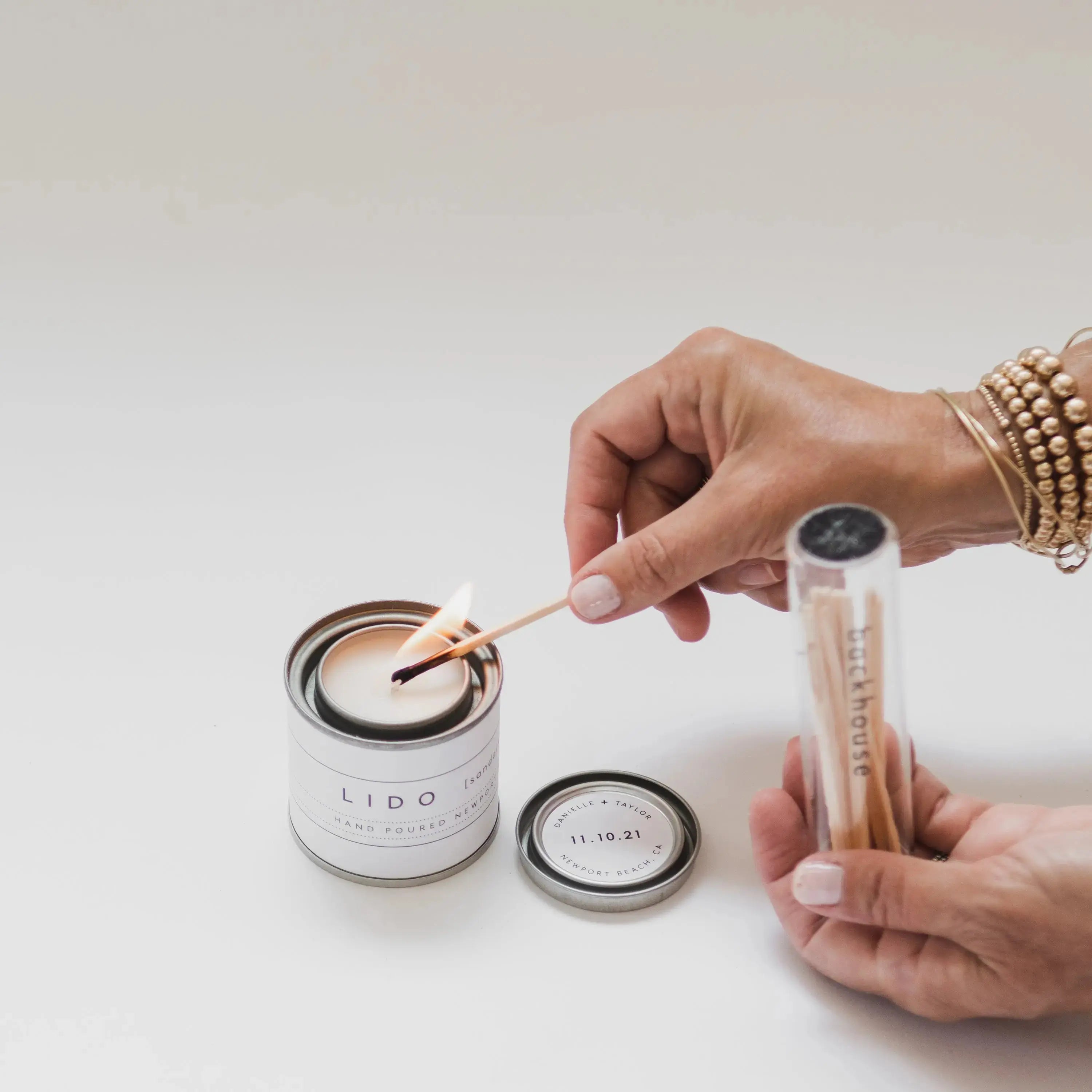 Hand lighting a Lido Newport custom hand-poured mini wedding candle favor featuring a personalized lid and a glass for a Newport Beach wedding.
